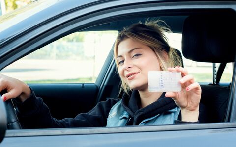 Junge frau im Autositzen präsentiert Ihren neu erworbenen Führerschein